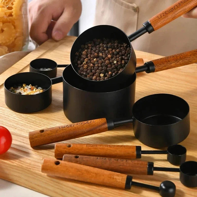 Black stainless steel measuring cups with wooden handles arranged on a wooden surface, featuring various sizes for baking and bartending.