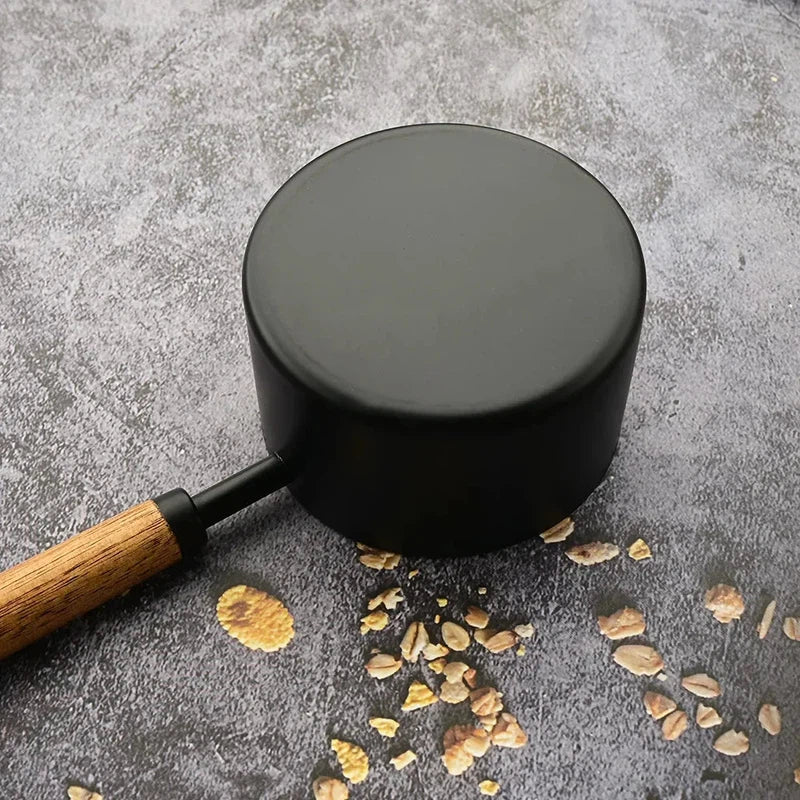 Black measuring cup with a wooden handle on a textured surface, part of an 8-piece stainless steel measuring tool set.