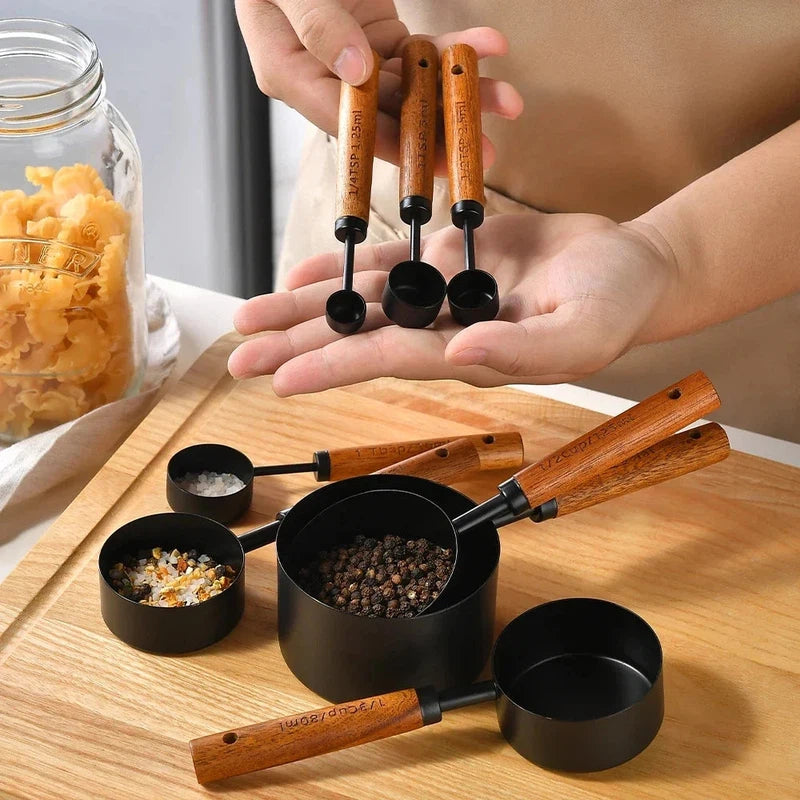 8-piece measuring cups with stainless steel and wooden handles, shown with spices and pasta on a wooden table.