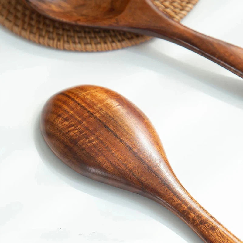 Wooden large spoon and fork cutlery set with long handles on a white surface.