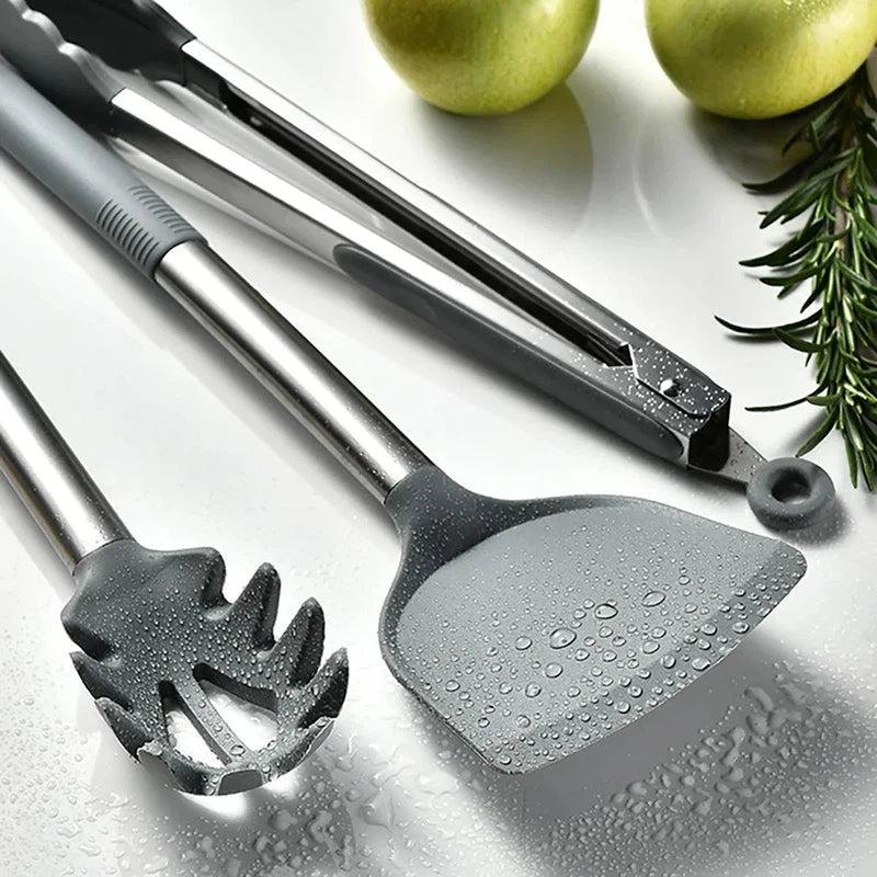 Silicone and stainless steel kitchen utensils set with spatula, soup spoon, and eggbeater on a counter.