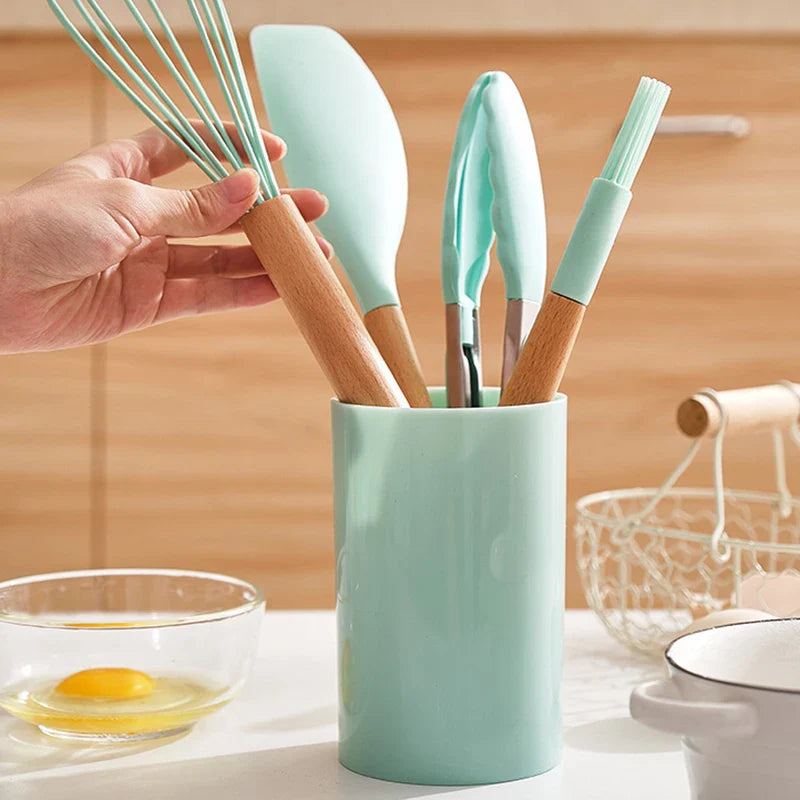 Non-stick silicone cookware utensils set with wooden handles, includes spatula, shovel, egg beaters in a countertop holder.