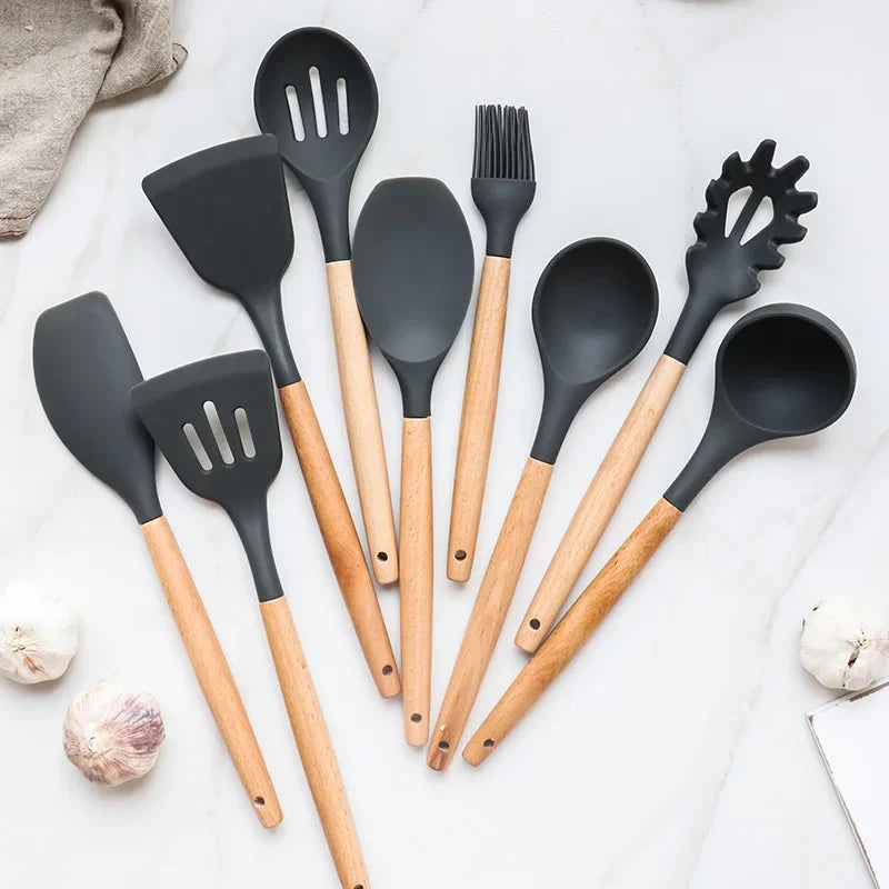 Non-stick silicone kitchen utensils set with wooden handles, including spatula, shovel, and egg beaters, displayed on a countertop.